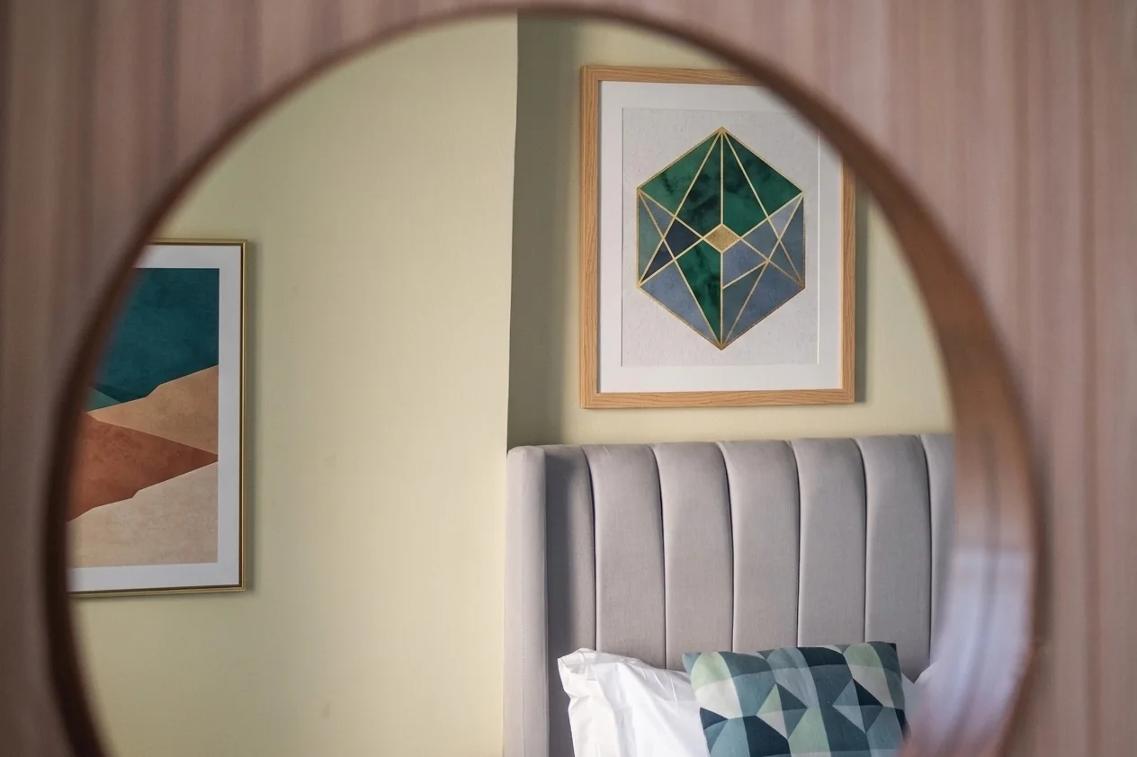 Dettaglio di uno specchio che riflette opere appese in una camera da letto
